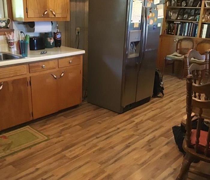 A kitchen that has wood laminate flooring that is buckling due to a leak from fridge