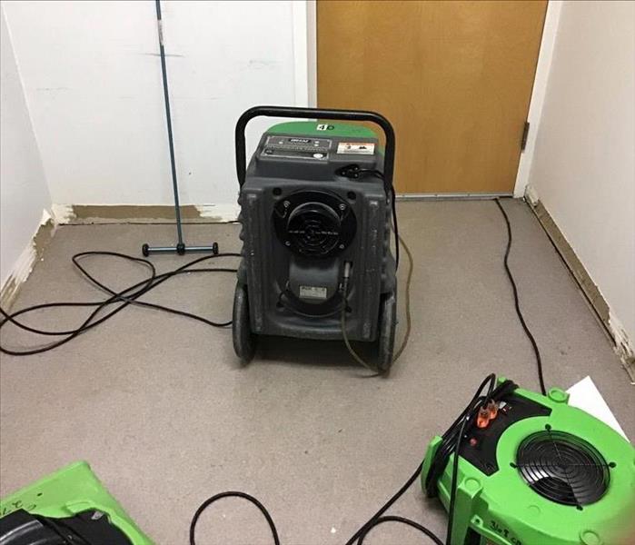 A closet with baseboards pulled and three green air movers and dehus