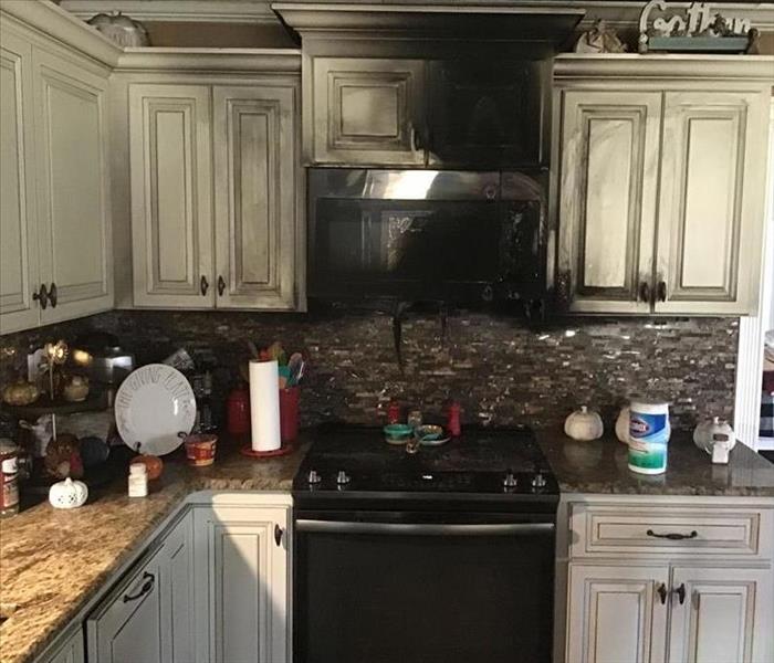 Kitchen with oven, microwave and tan cabinets covered in black smoke