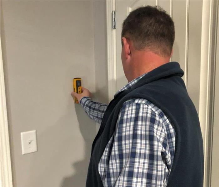 A male holding a protemeter against a wall checking to see if there is moisture.