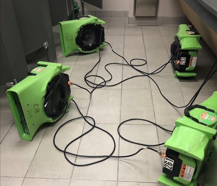 Five green air movers sitting on a tile floor in a bathroom