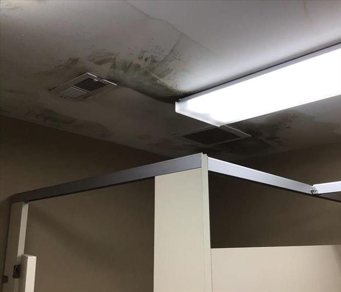 A bathroom stall with an air vent above it, and water pooling above it.